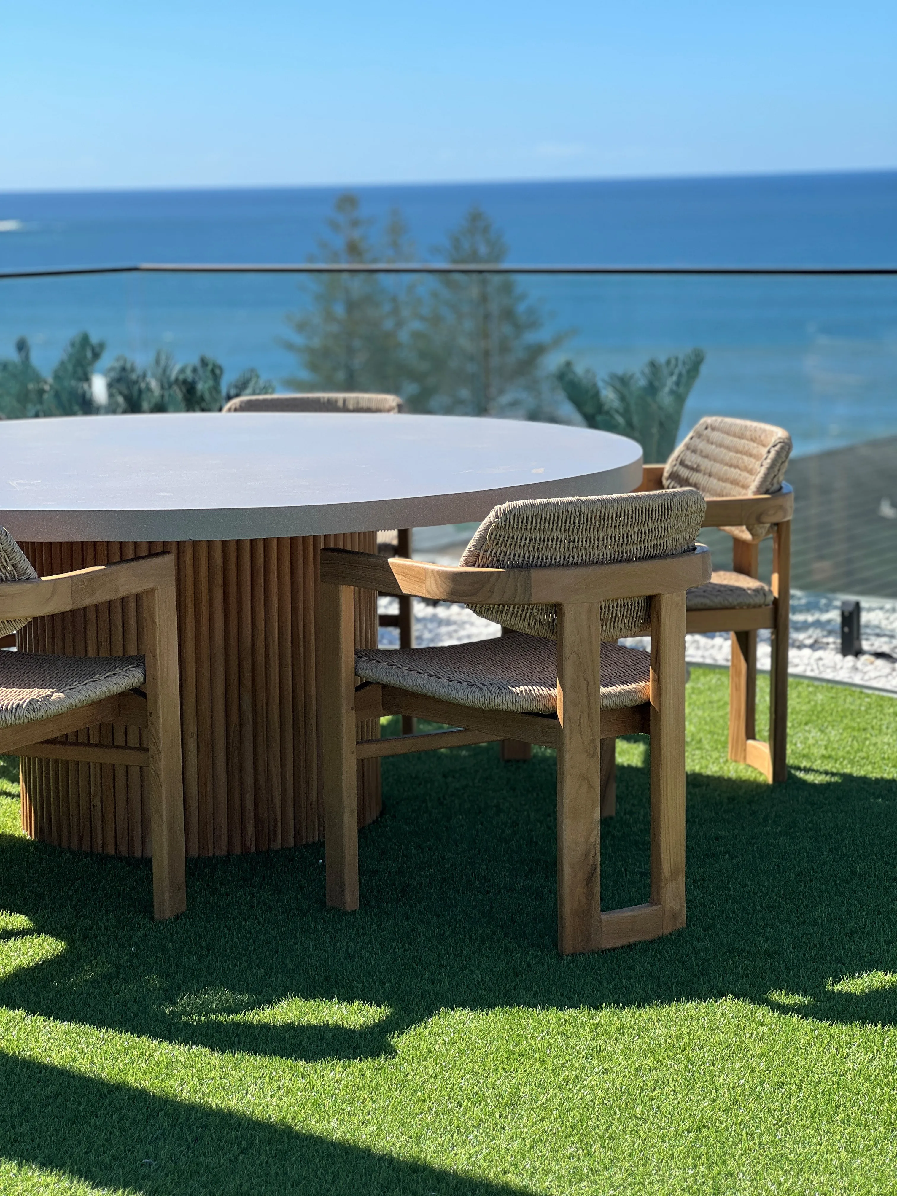 Rooftop dining with round concrete table, rope-woven teak chairs and ocean views